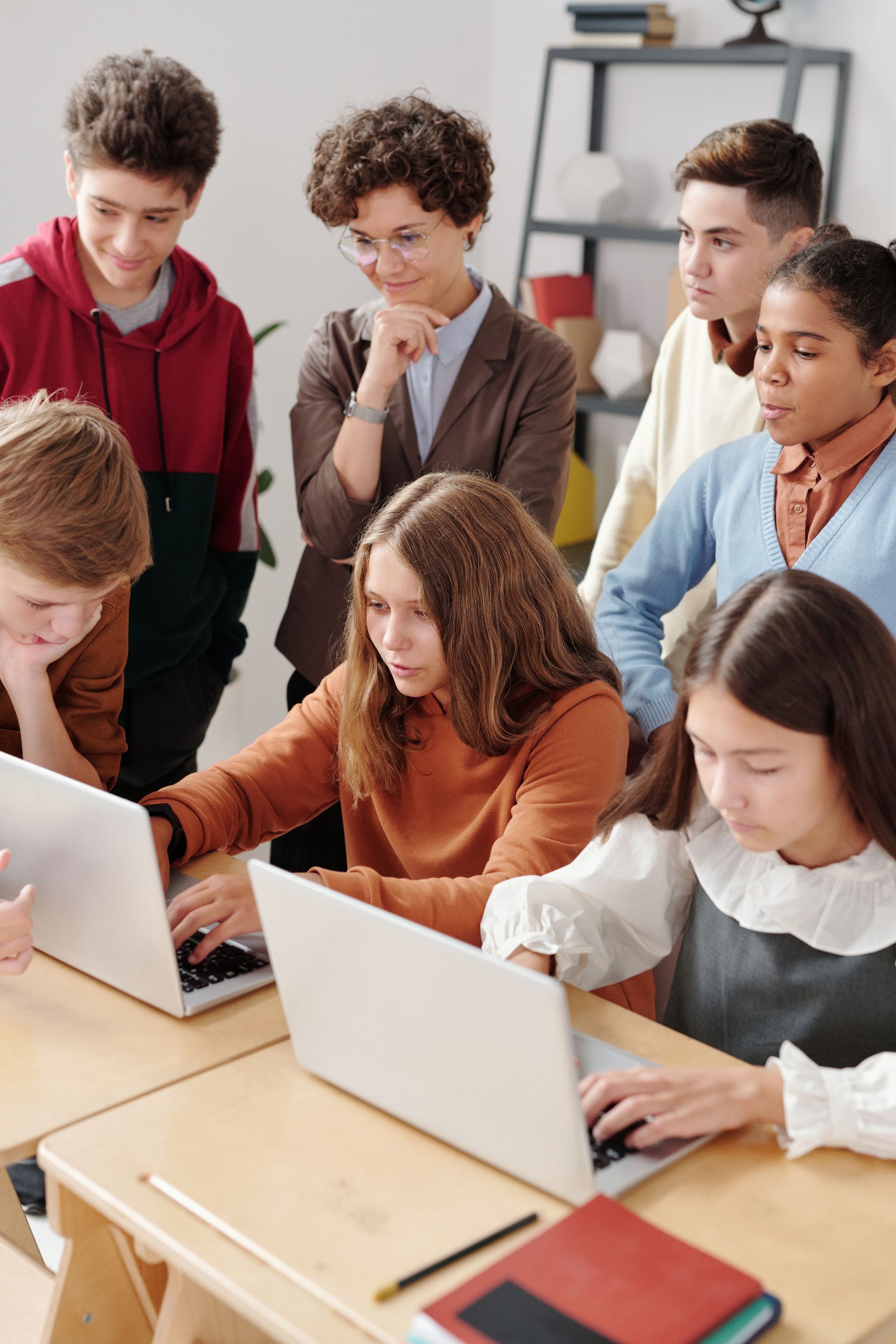 Three teenagers working together on a laptop in a classroom.
